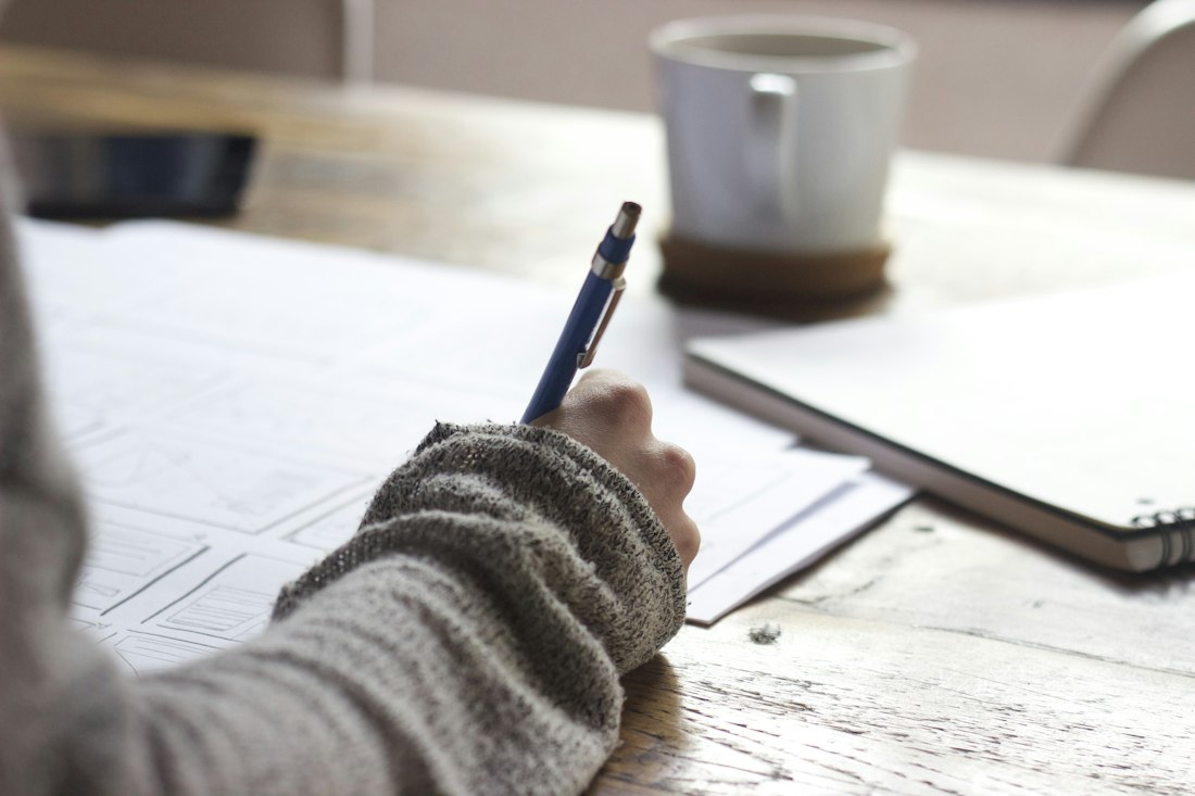 Taking handwritten notes at a desk with a notebook and a cup